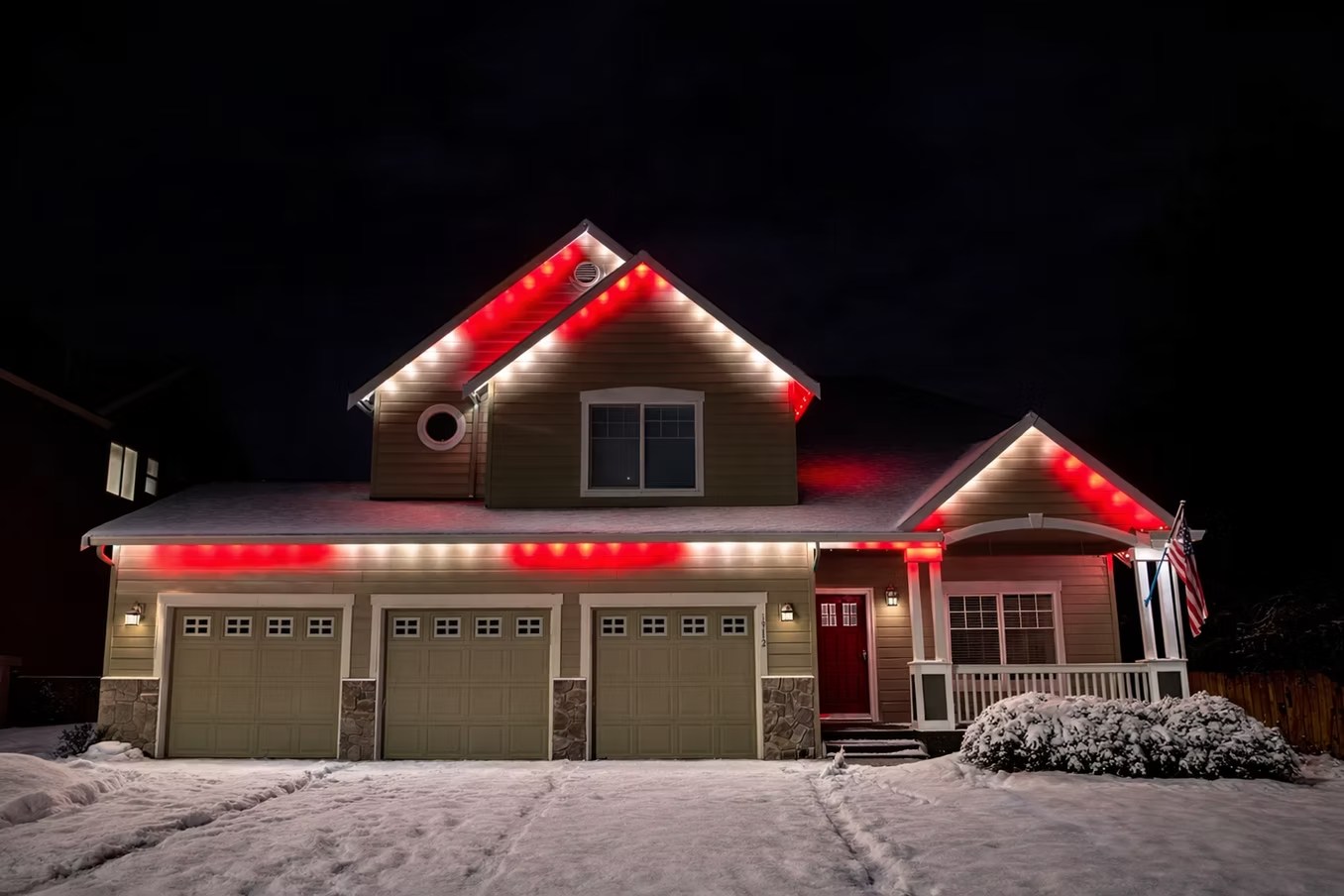 Red and white roofline lights on a two-story home with snow on the driveway